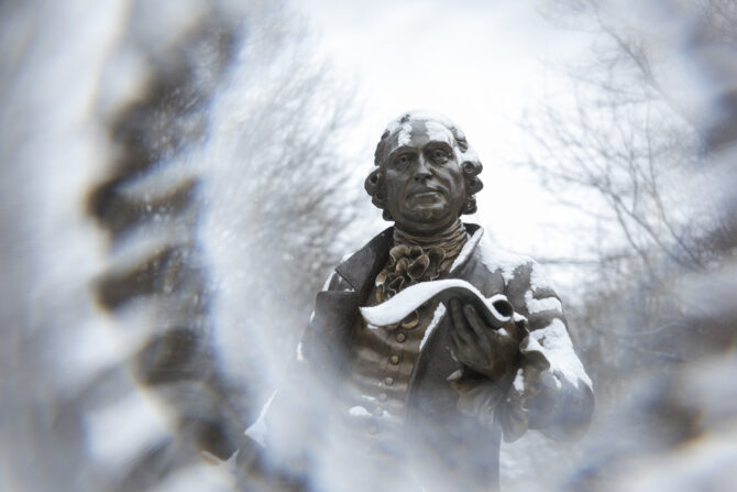 Snow falling on a statue of George Mason statue at the George Mason University Fairfax campus.