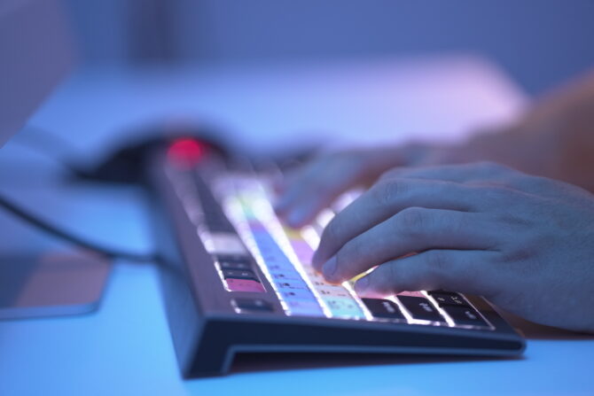 Close-up of hands typing on a backlit keyboard with multicolored keys.