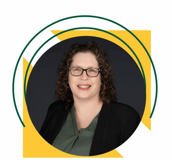 Professional headshot of a middle-aged woman with shoulder-length curly brown hair wearing glasses, a green blouse, and a black blazer.