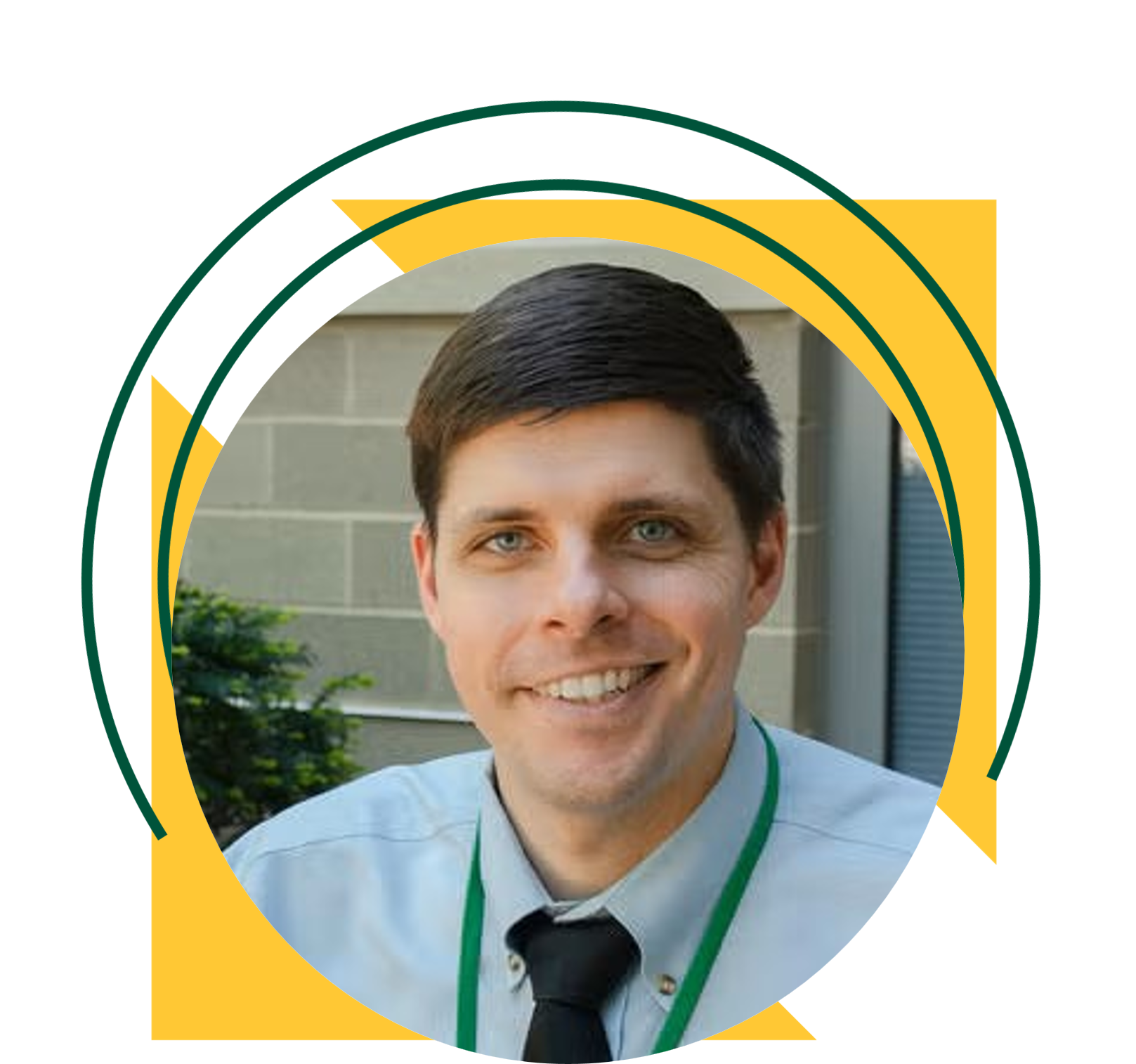 A man smiling wearing a light blue dress shirt, dark tie, and green lanyard stands outdoors in front of a campus building. The portrait is framed within a circular design accented by yellow triangles and green curved graphic elements.